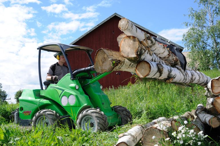 A compact loader lifting logs with a log grabbing attachment.