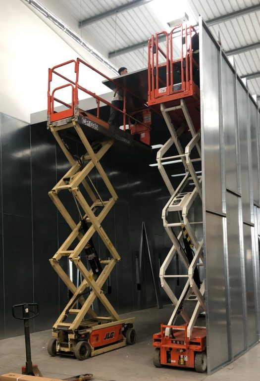 Two scissor lifts being operated in tandem. Both scissors feature large working platforms.